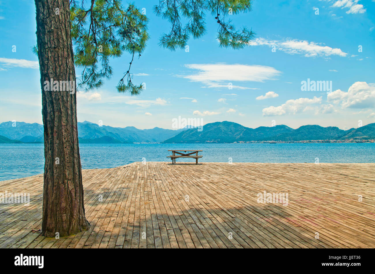 Tavolo in legno con panche sul piatto di legno la piattaforma a Mare Egeo con big pine tree in primo piano sulla giornata di sole a Marmaris, Turchia Foto Stock