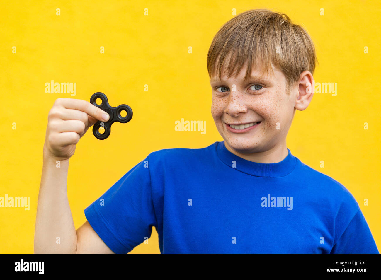 Giovane bella felice ragazzo con lentiggini blu t-shirt holding agitano: spinner su sfondo giallo. Foto Stock