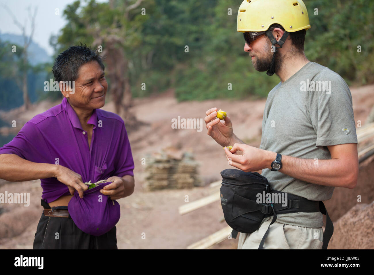 Un uomo offre a Robert Hahn un aspro frutto dalla sacca della sua maglietta sulla riva del fiume Nam Ou in Ban Phu Muang, Laos. Foto Stock