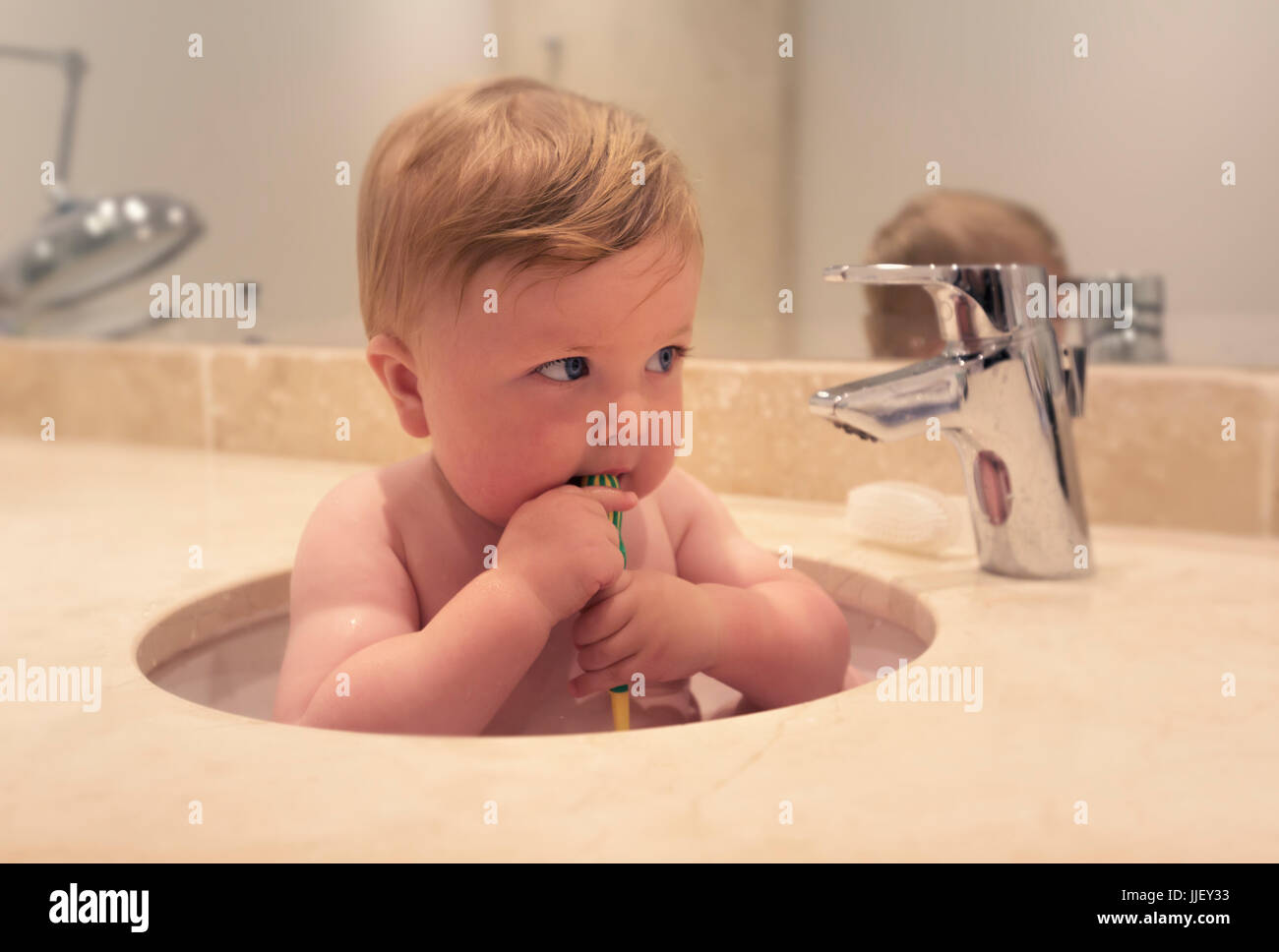 Bambino seduto in un lavandino spazzolando i suoi denti Foto Stock