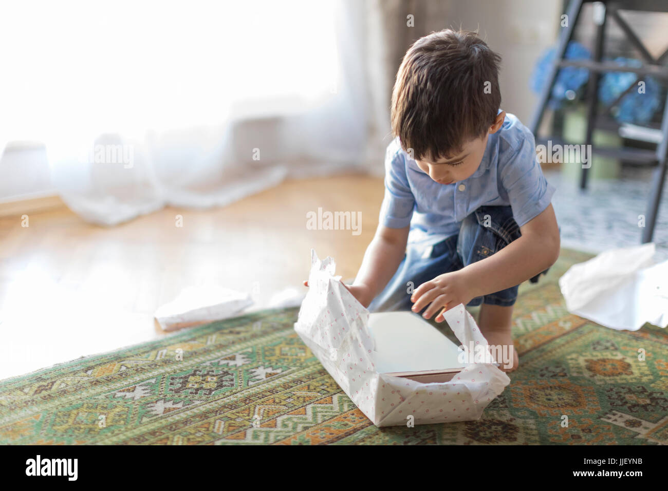 Ragazzo seduto sul pavimento scartare un regalo di compleanno Foto Stock