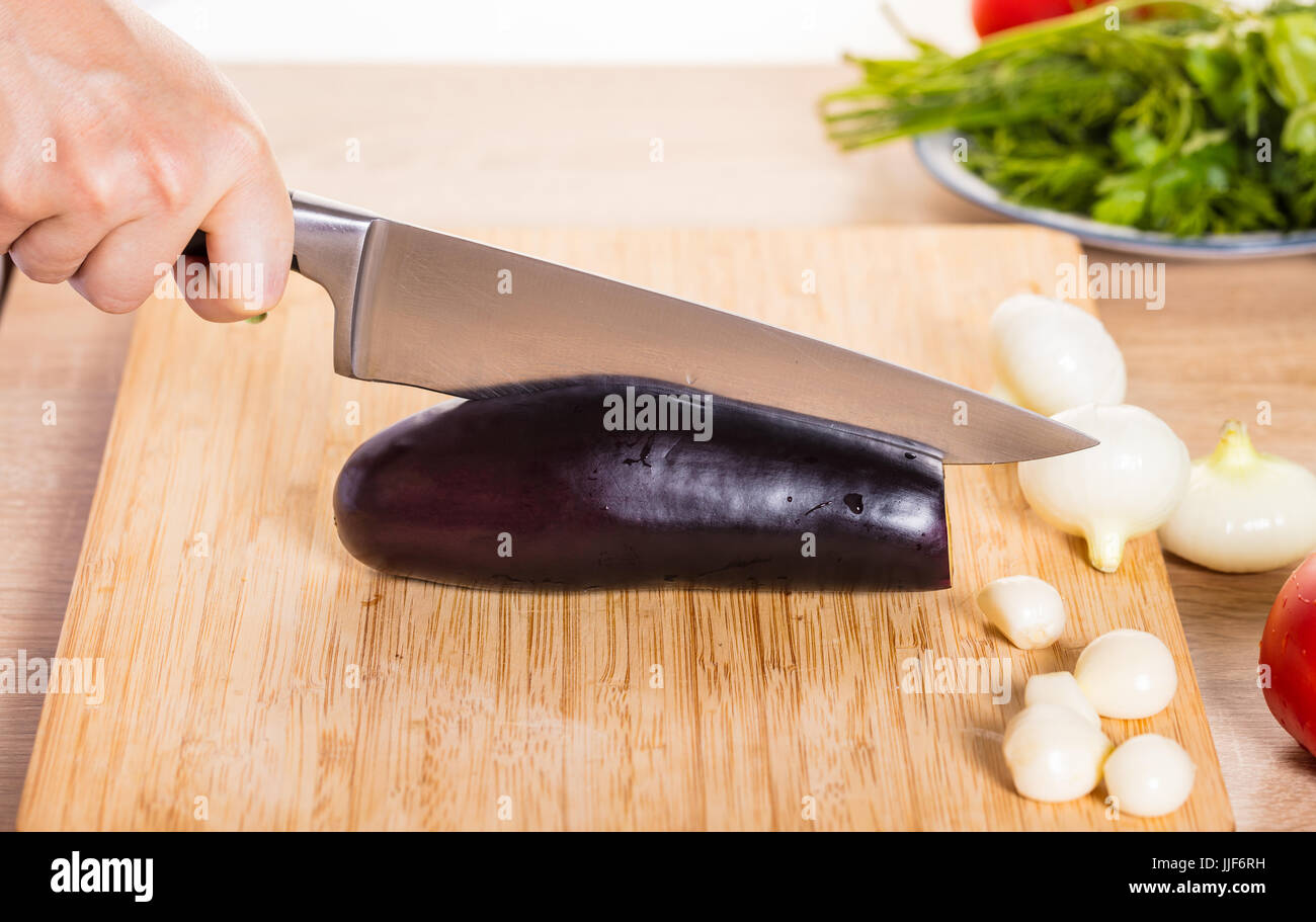 Il cuoco taglia le melanzane con un coltello Foto stock - Alamy
