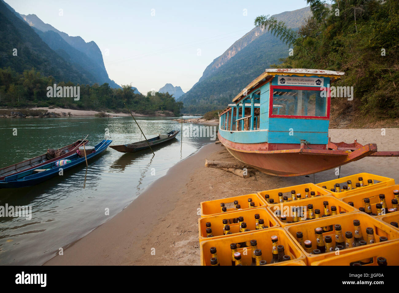 Barche e una grande pila di vuoto birra Lao (la birra nazionale) sulla riva del fiume Nam Ou in Muang Ngoi, Laos. La birra è il combustibile necessario per la vivace traffico turistico centrata intorno alla città. Foto Stock