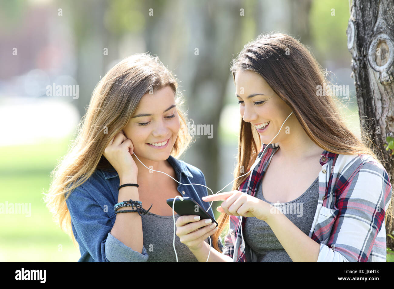 Due lieti teen amici ascoltando la condivisione della musica di auricolari e smartphone in un parco Foto Stock