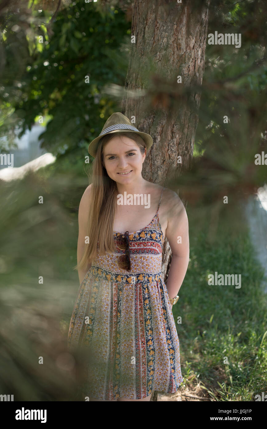 Donna sorridente in piedi in park appoggiato a un albero Foto Stock