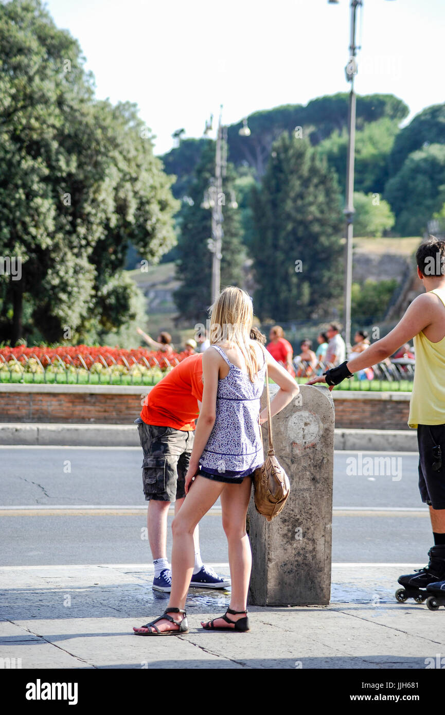 Giovani turisti guardano per scambiatore di calore a un acqua potabile fontana di fronte al Colosseo in una vivace giornata di sole. Roma Italia Foto Stock