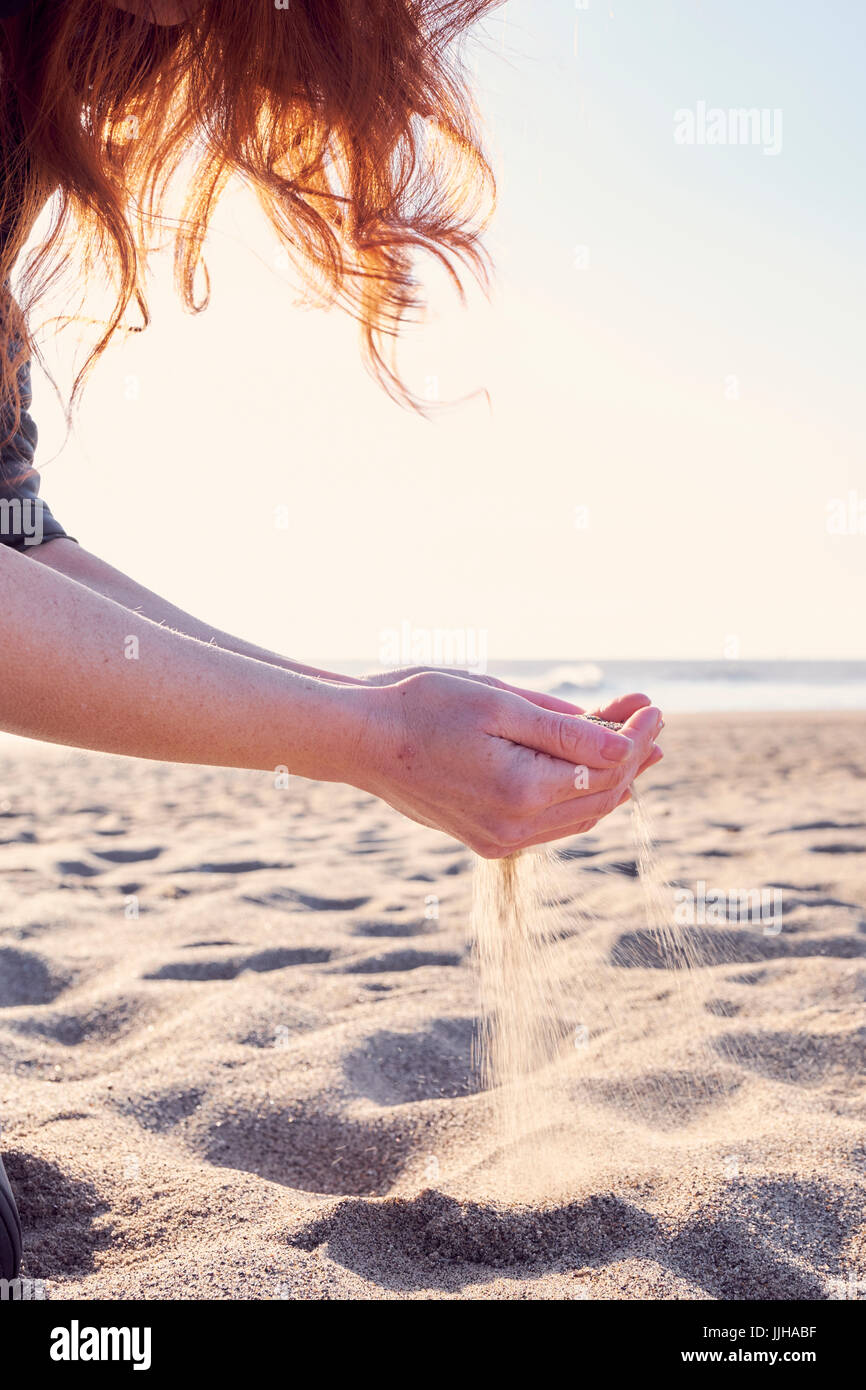 Una giovane donna di vagliatura sabbia attraverso le mani sulla spiaggia. Foto Stock