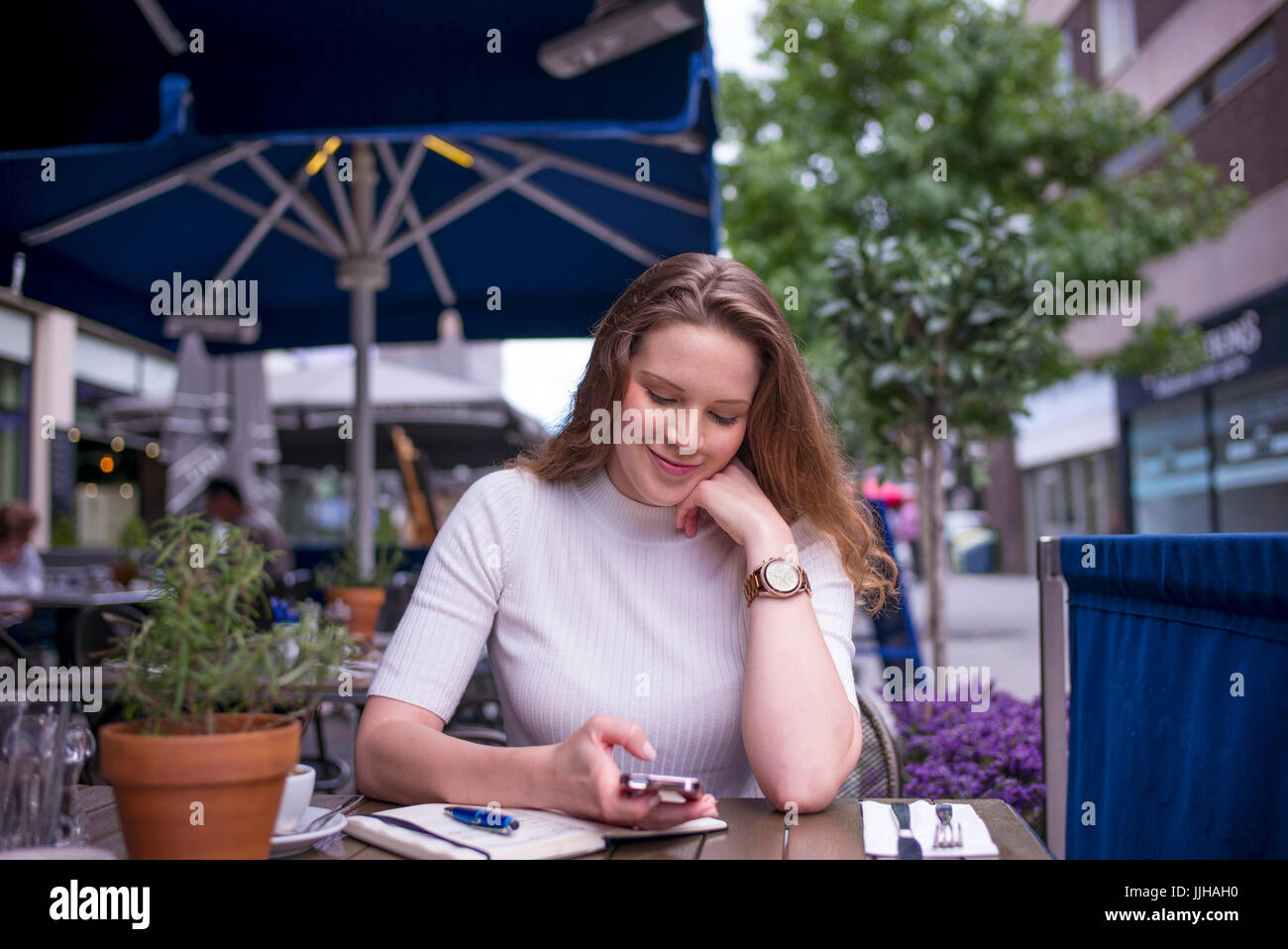 Una giovane donna controlla il suo telefono mentre seduto fuori ad un cafe. Foto Stock