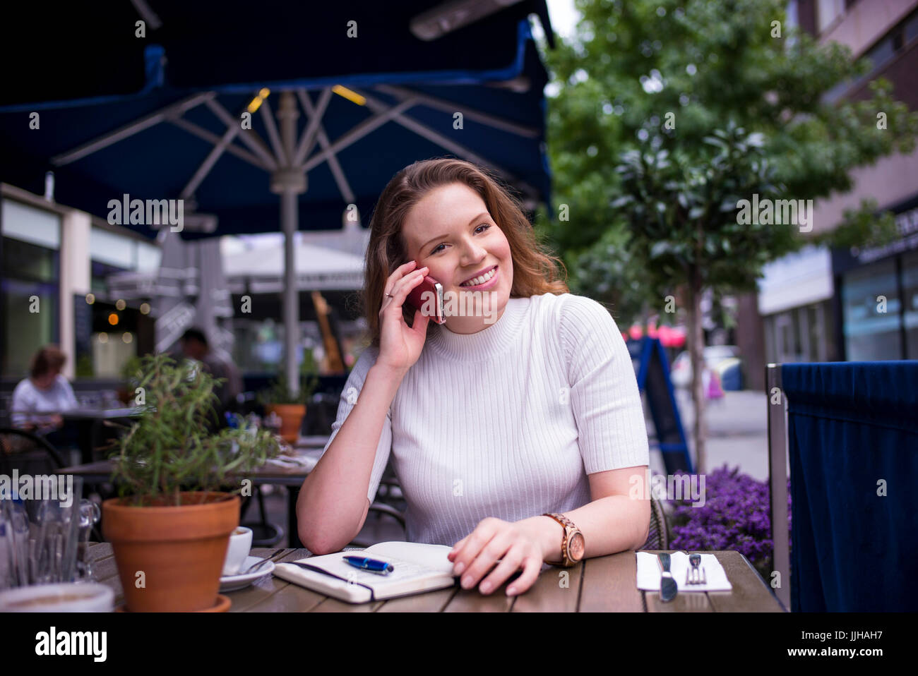 Una giovane donna parla sul suo telefono mentre seduto fuori ad un cafe. Foto Stock