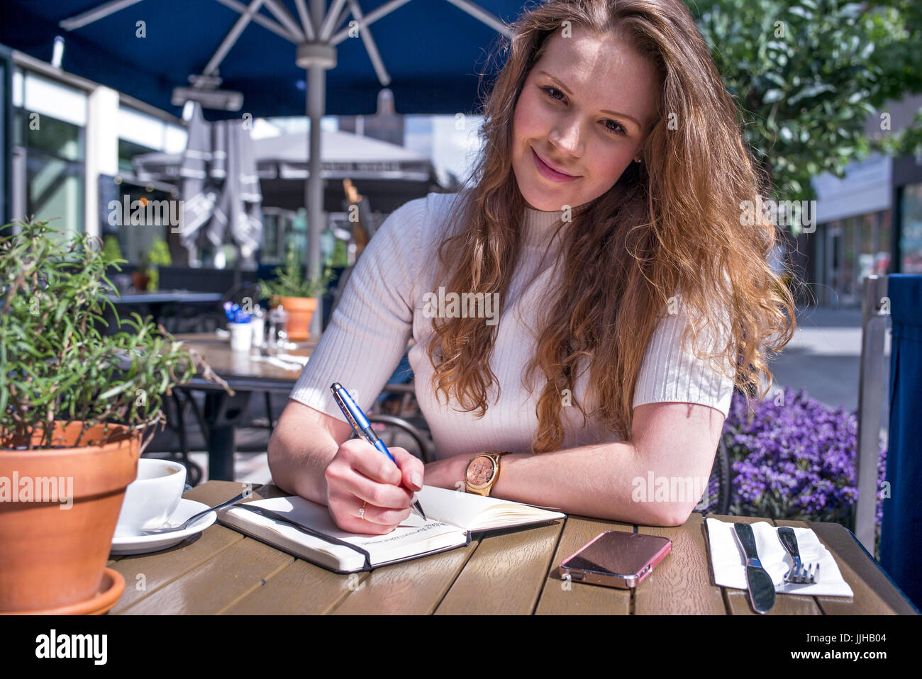 Una giovane donna seduta al di fuori di un cafe prendendo alcune note. Foto Stock