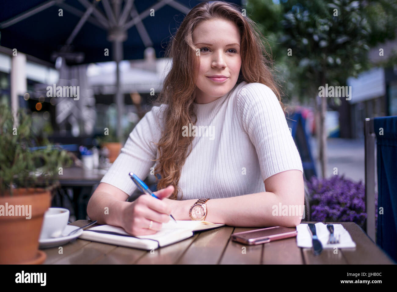 Una giovane donna seduta al di fuori di un cafe prendendo alcune note. Foto Stock