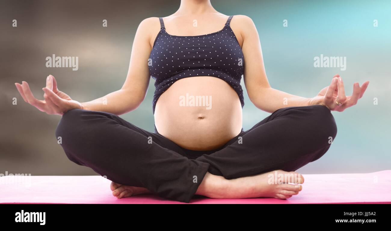 Donna incinta metà sezione meditando contro blu sfocate sfondo marrone Foto Stock