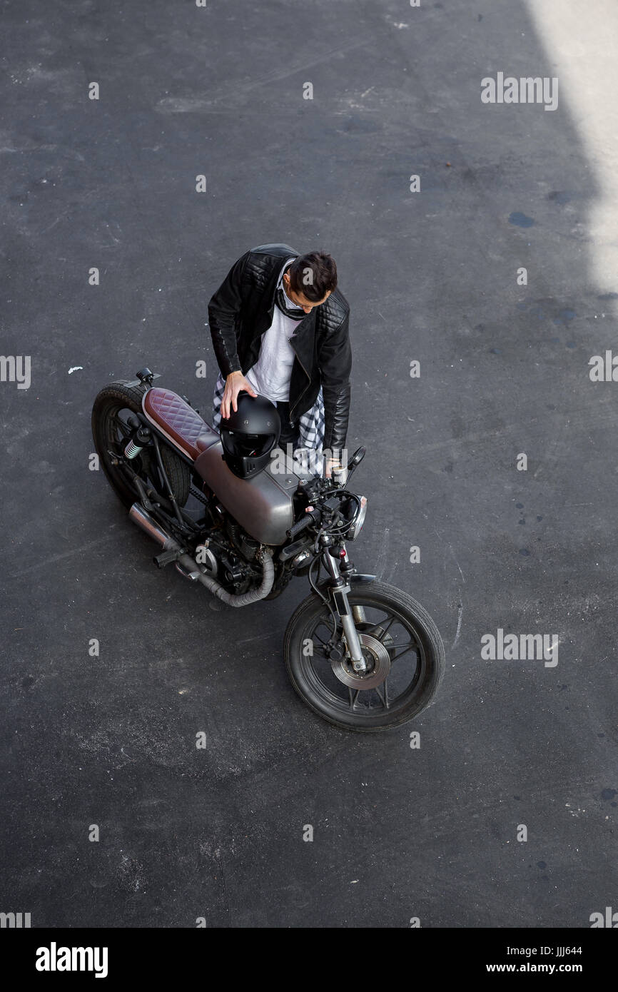 Vista dall'alto di un bel ragazzo motociclista in cuoio nero biker giacca e camicia a scacchi a controllare il suo classico stile Café Racer motocicletta. Moto custom made in Foto Stock