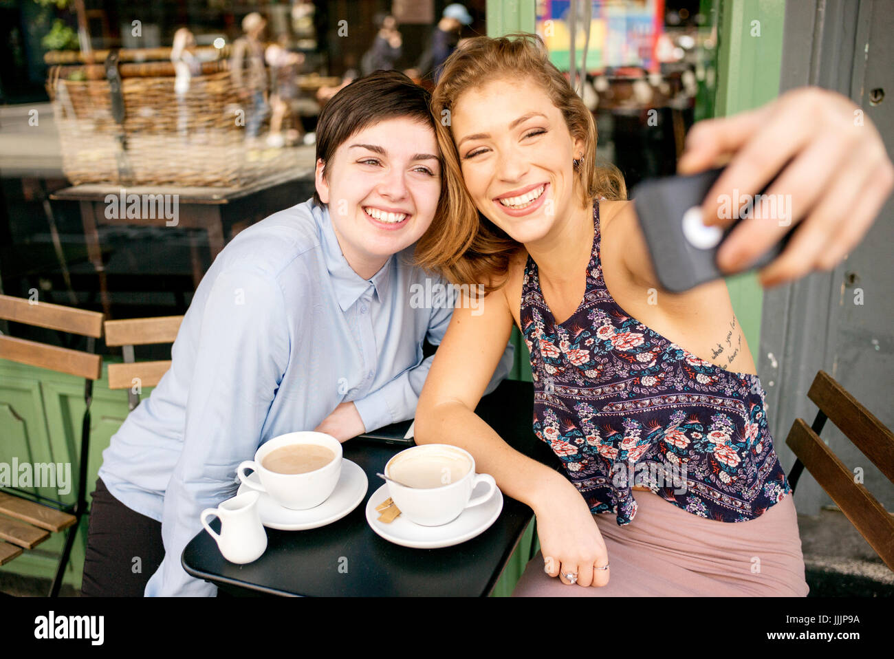 Una giovane coppia lesbica prendere un selfie al di fuori di un coffee shop. Foto Stock