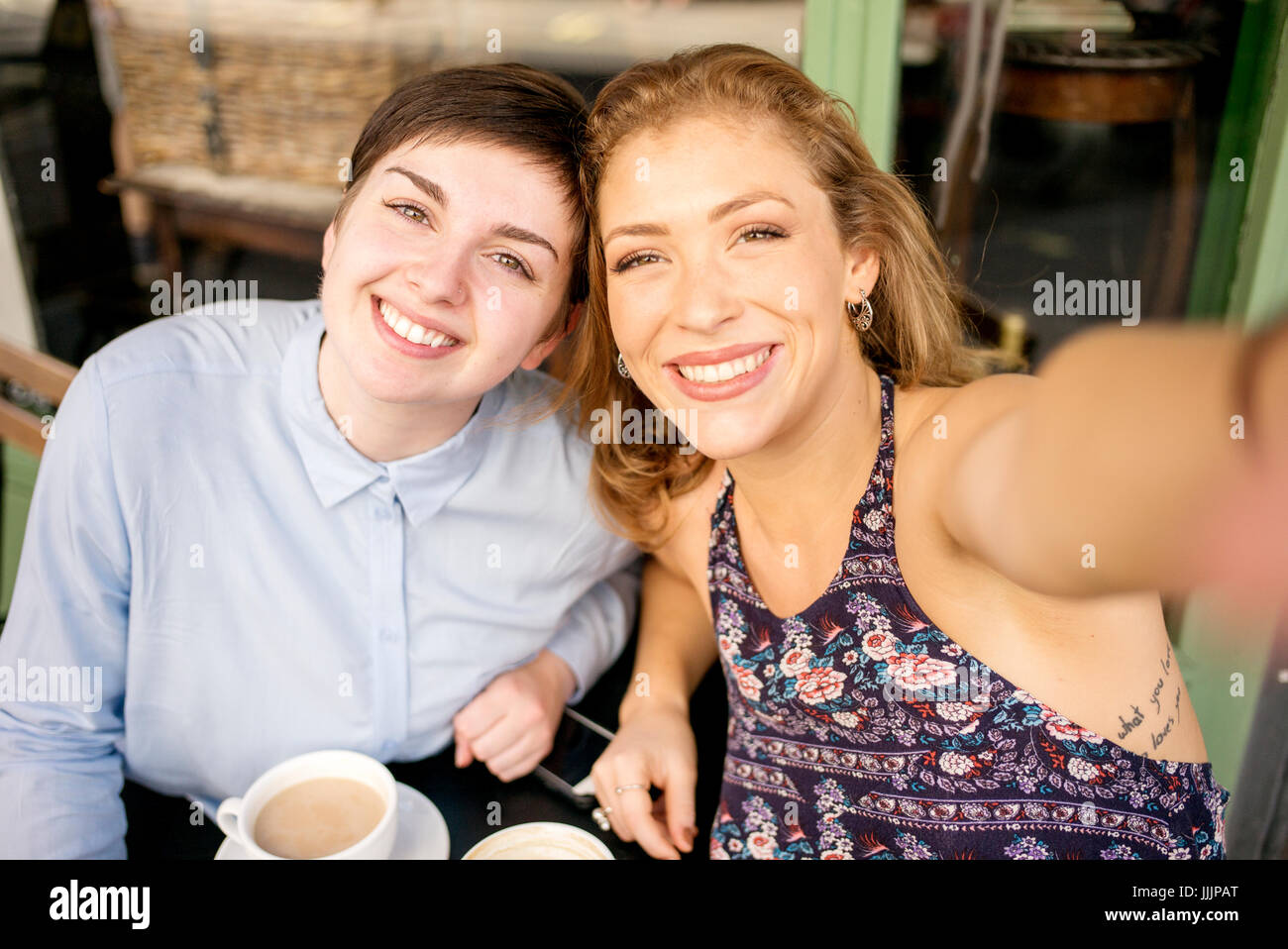 Una giovane coppia lesbica prendere un selfie al di fuori di un coffee shop. Foto Stock
