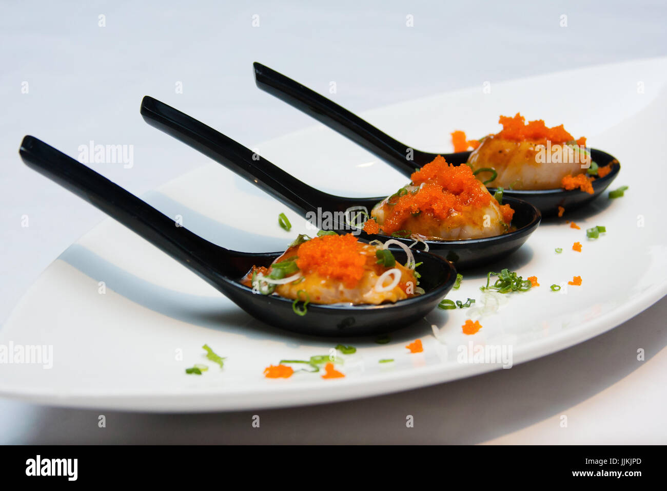 Capesante su cucchiaio nero guarnita con uova di pesce Foto Stock