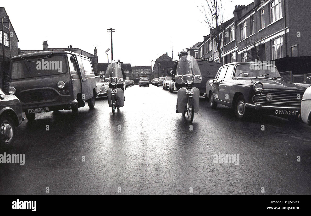 1974, Londra Sud, due femmine operai del traffico di pattuglia corsa giù per una strada di automobili parcheggiate e furgoni sul loro nuovo modo di trasporto per la loro applicazione della legge il lavoro, piccoli ciclomotori agile. Foto Stock