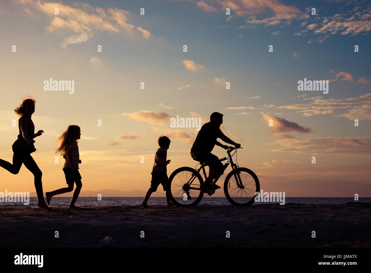 Padre e figli giocando sulla spiaggia al tramonto. Concetto di famiglia amichevole. Foto Stock