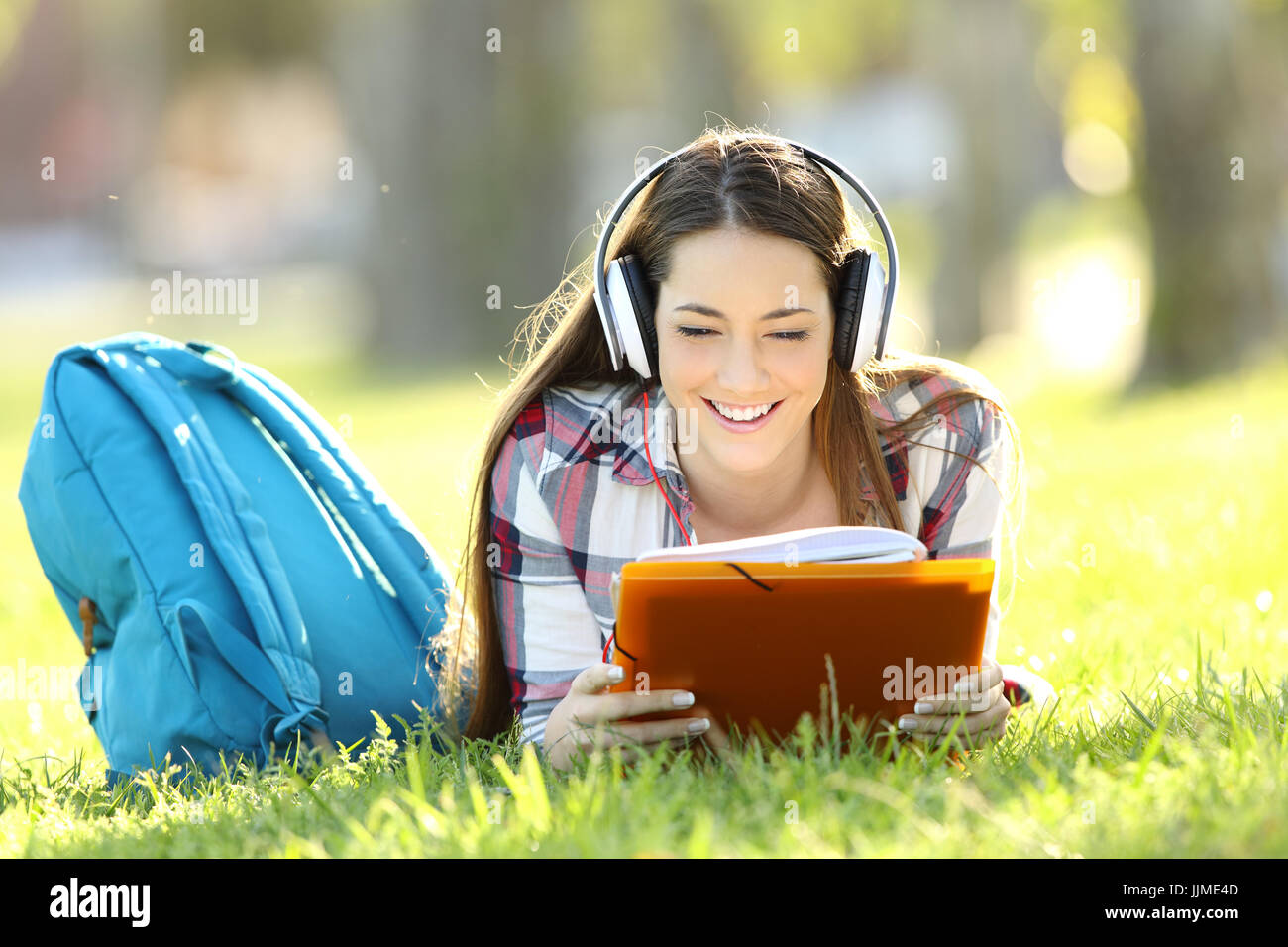 Vista frontale ritratto di uno studente note di lettura e ascolto di un audio tutorial sulla linea giacendo sul prato di un parco Foto Stock