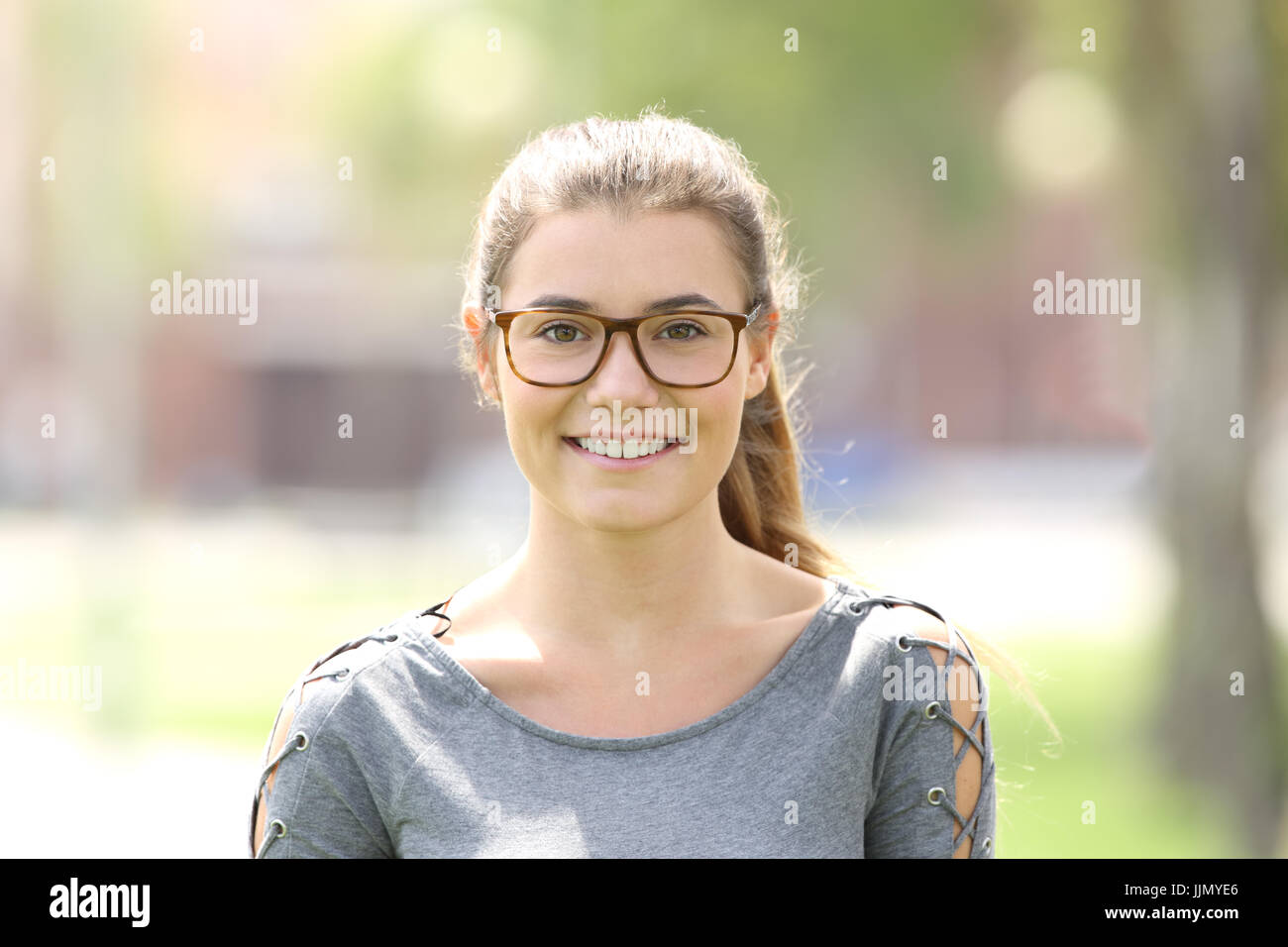 Ritratto di una ragazza che indossa occhiali che vi guardano all'aperto in un parco Foto Stock