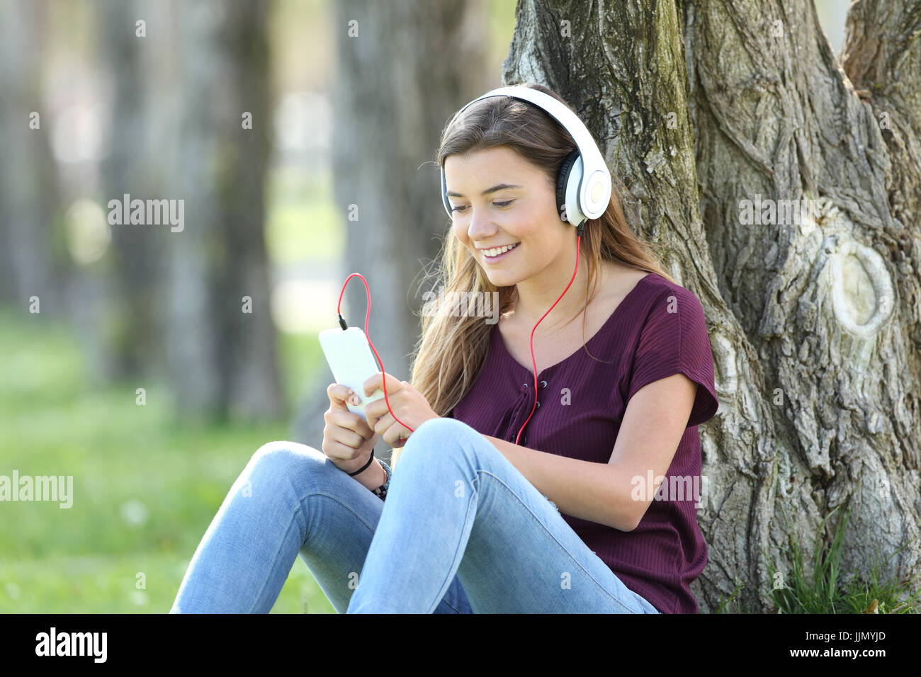 Single teen ascoltare musica on line con le cuffie e smart phone seduta sul prato di un parco Foto Stock