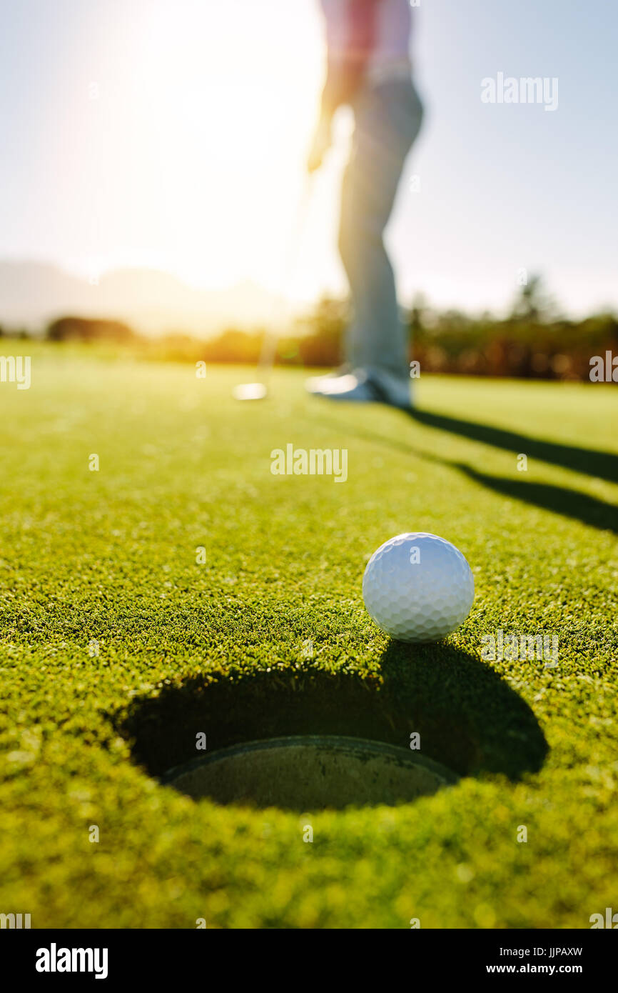 Pallina da Golf in corrispondenza del bordo del foro con il giocatore in background. Professional Golfer mettendo la sfera nel foro in una giornata di sole. Foto Stock