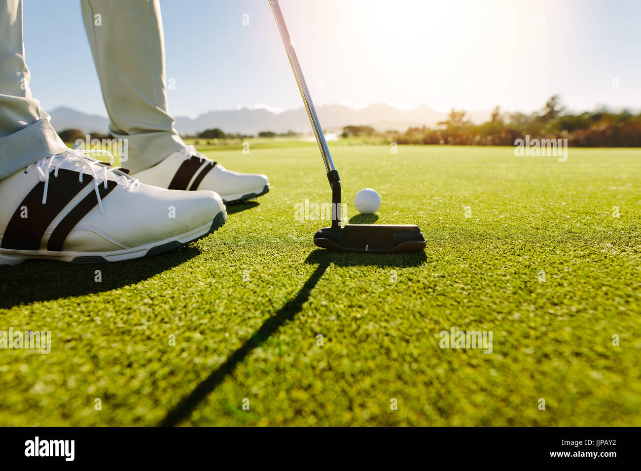 Golfista maschio sul putting green circa per scattare la foto. Giocatore di golf putting pallina da golf a foro. Foto Stock