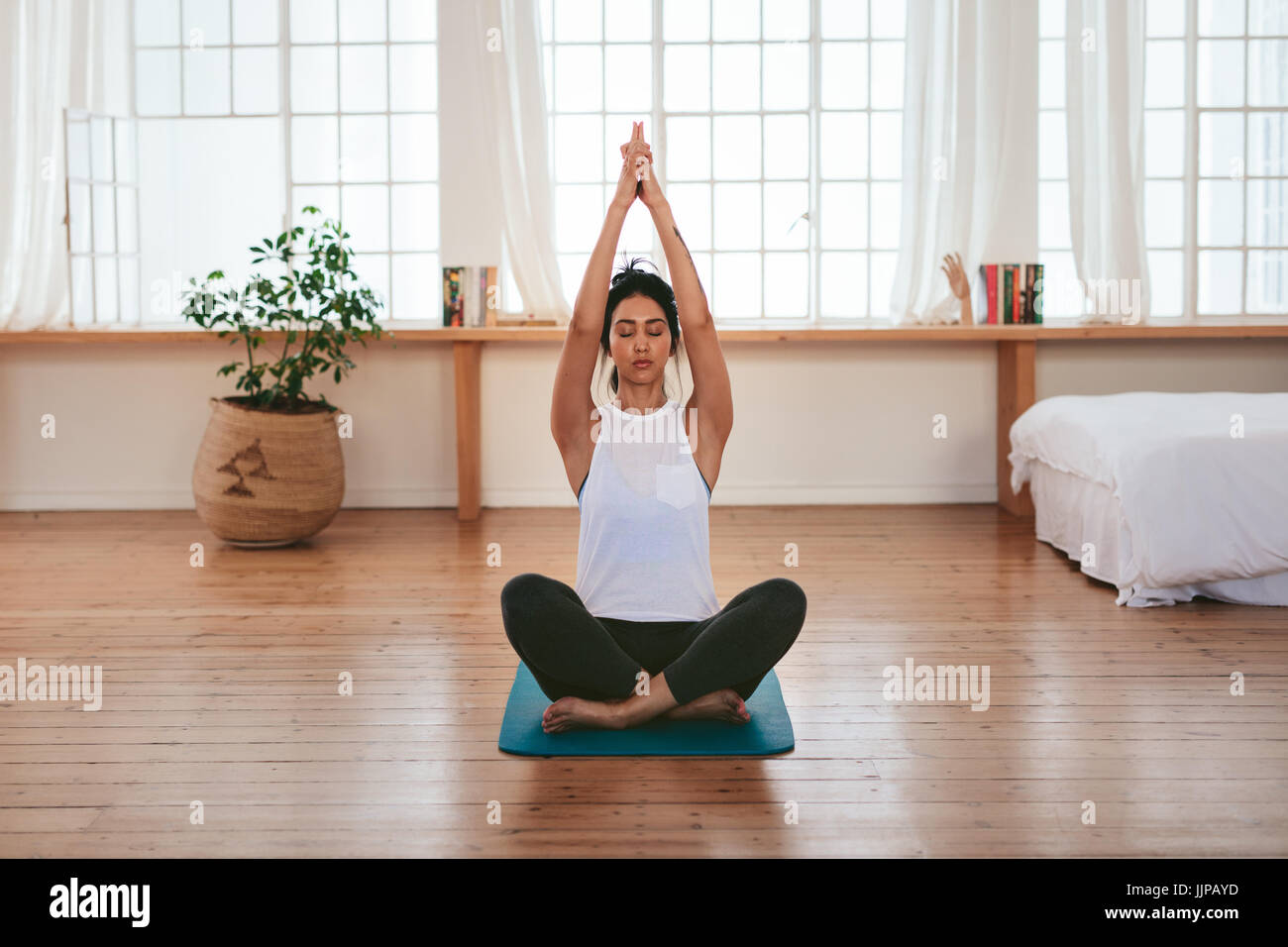 A piena lunghezza shot di sana e bella giovane donna seduta a casa in posizione di yoga. Femmina Fitness seduto con le mani giunte sopra la sua testa. Foto Stock