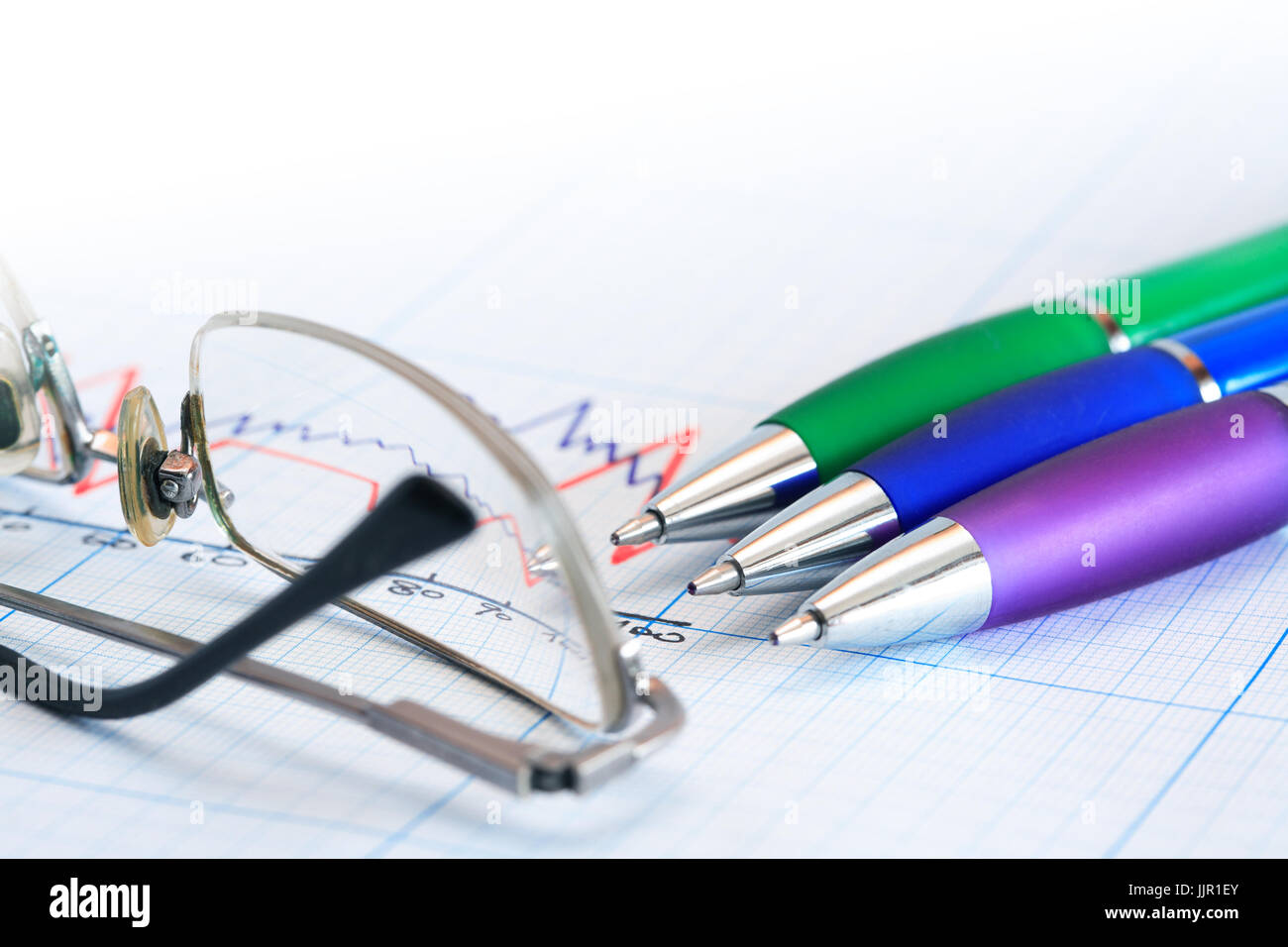 Extreme closeup di alcune penne dei colori nei pressi di occhiali su un foglio di carta millimetrata con sfondo grafico Foto Stock