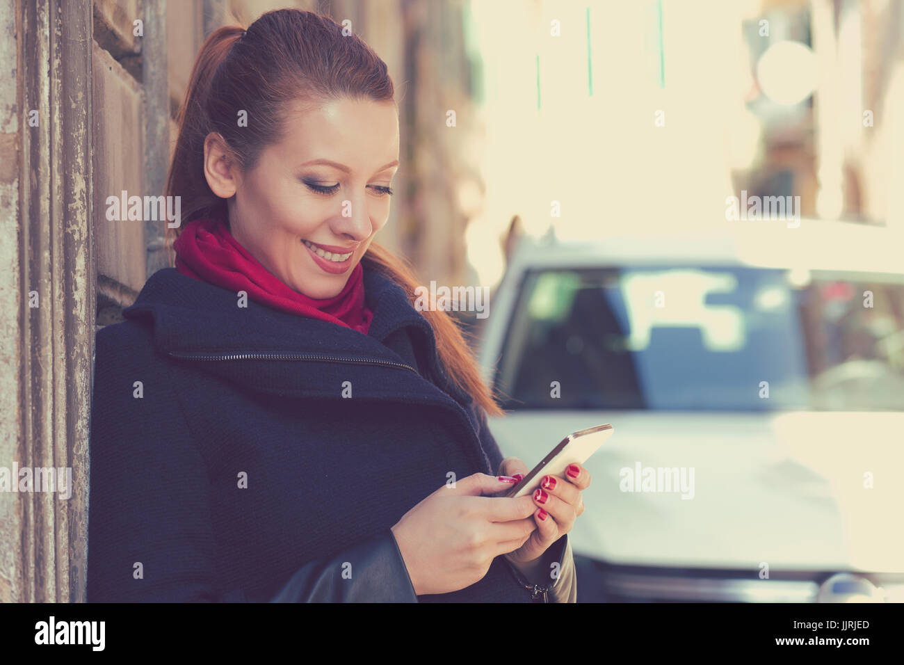 Donna sorridente con un cellulare all'aperto in piedi accanto alla sua nuova vettura texting. Foto Stock