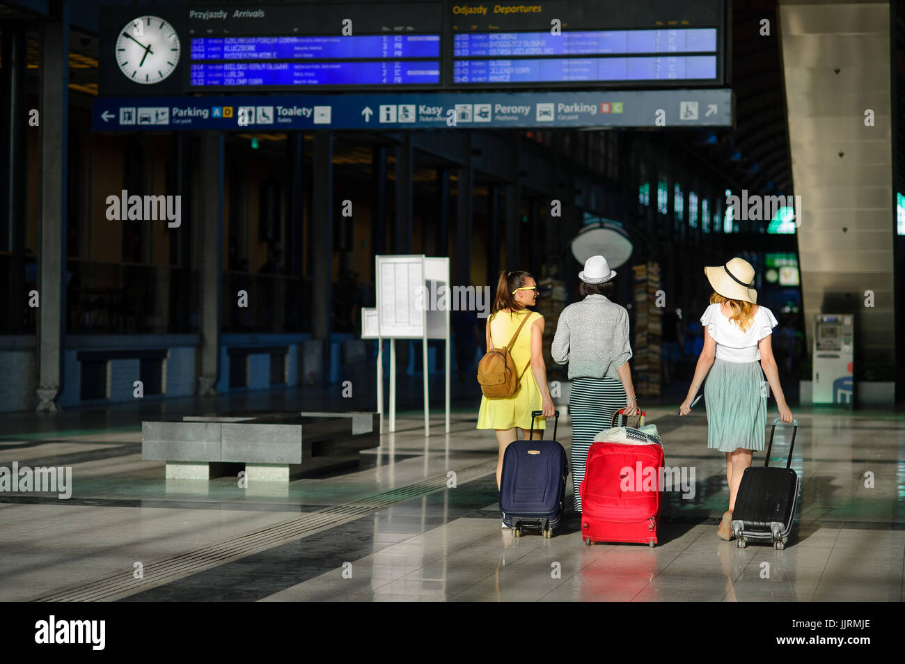 Un gruppo di ragazze alla stazione ferroviaria. I turisti con i loro bagagli stanno correndo ai ripari per il loro treno. Vista posteriore. Tempo di vacanze estive. Foto Stock