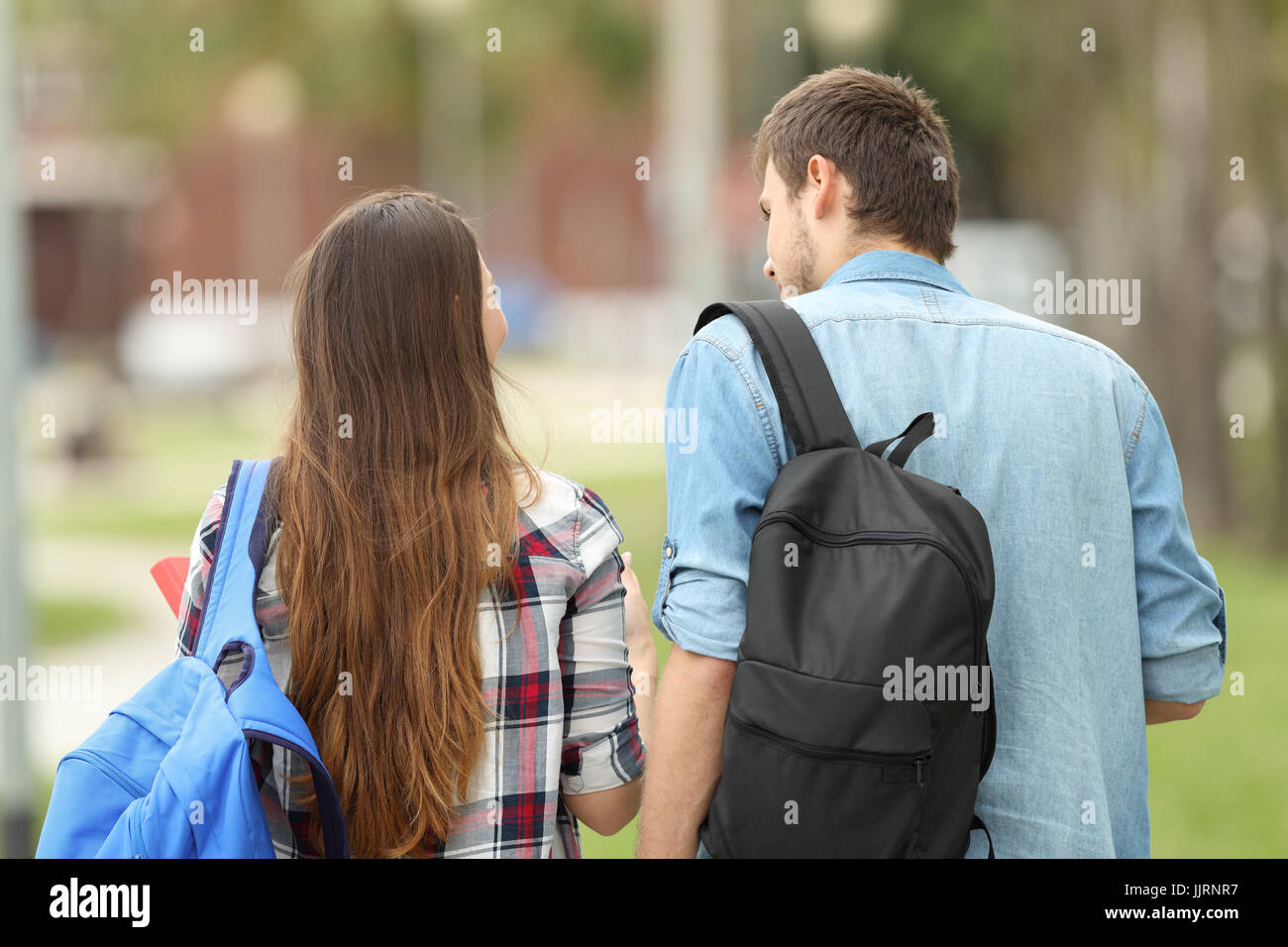 Vista posteriore del ritratto di due studenti borse e zaini camminare e parlare in un parco Foto Stock