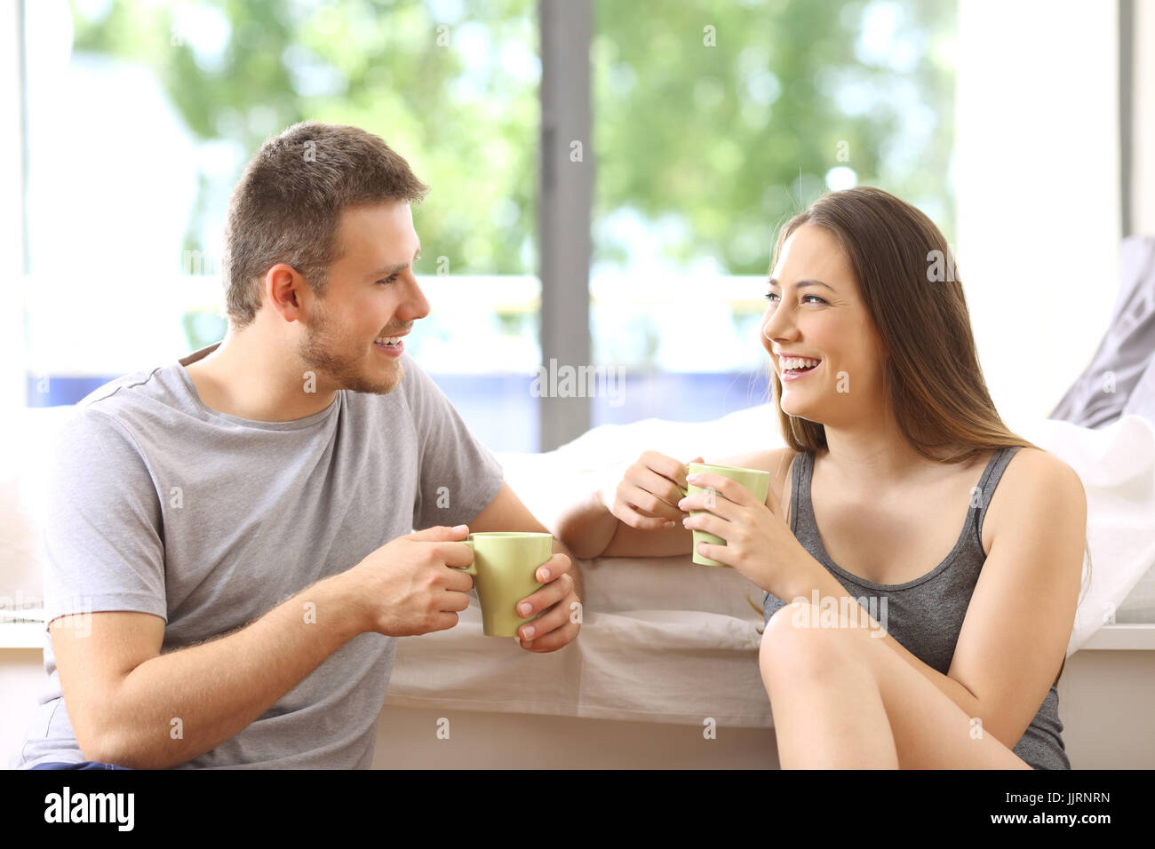 Coppia felice di parlare e di avere la prima colazione in una camera di hotel o a casa con uno sfondo verde all'aperto Foto Stock
