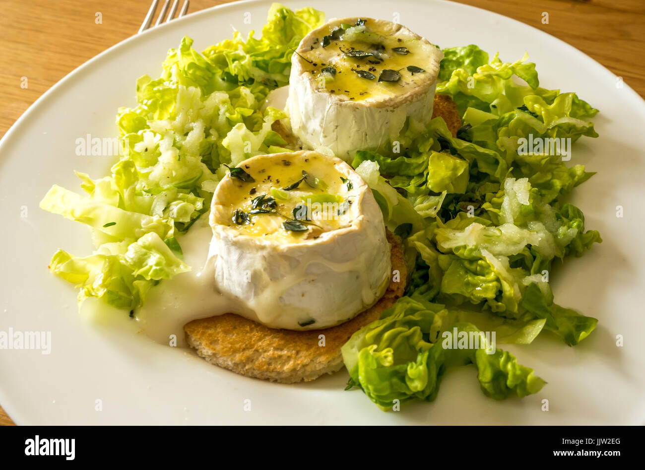 Insalata calda con formaggio di capra su letto di piccolo gioiello lattuga, olio di noce, pane tostato, mela grattugiata e succo di limone medicazione cosparsi di timo Foto Stock
