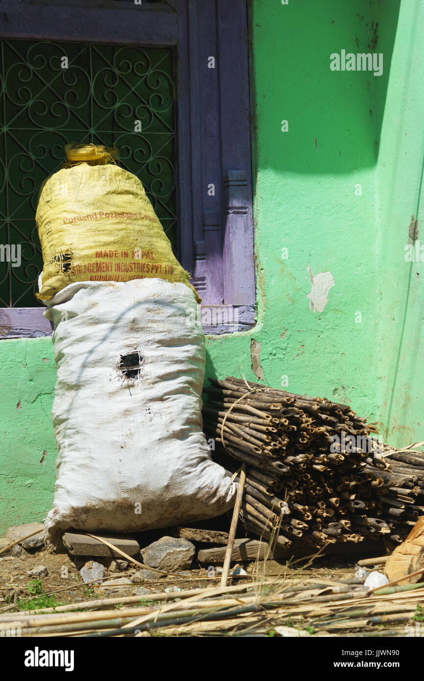 Sacchi riempiti con materiale di costruzione e fascio di steli di bambù di fronte a una casa. Villaggio di tal, regione di Annapurna, Nepal. Foto Stock