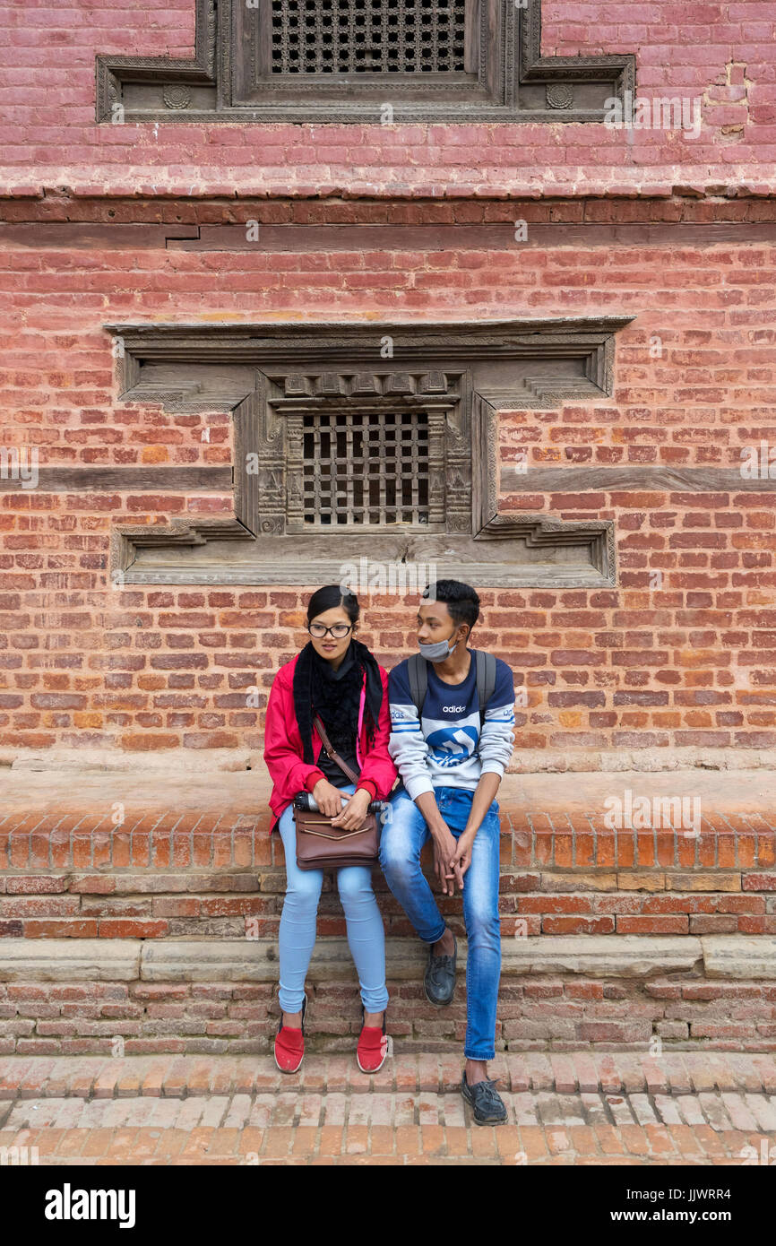 Giovani nepalesi giovane vestito in abiti moderni seduto davanti a un antico edificio in Durbar Square, Kathmandu Foto Stock