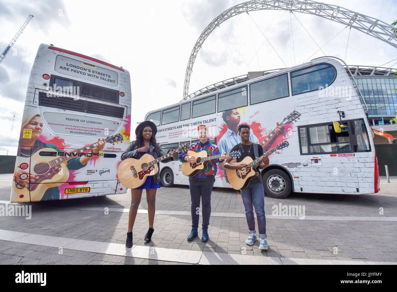 Londra, Regno Unito. Il 21 luglio 2017. Musicisti (L a R) Modupe Obasola, Kal Lavelle e Jay Johnson, che hanno preso parte al sindaco di Londra del musicista di strada annuale competizione, sostare di fronte gli autobus con le loro immagini. Dire Straits frontman Mark Knopfler svela due iconico London bus esterni al Wembley Stadium per festeggiare il lancio di concerti, in associazione con Gibson, alla vigilia del musicista di strada internazionale giorno. Credito: Stephen Chung / Alamy Live News Foto Stock
