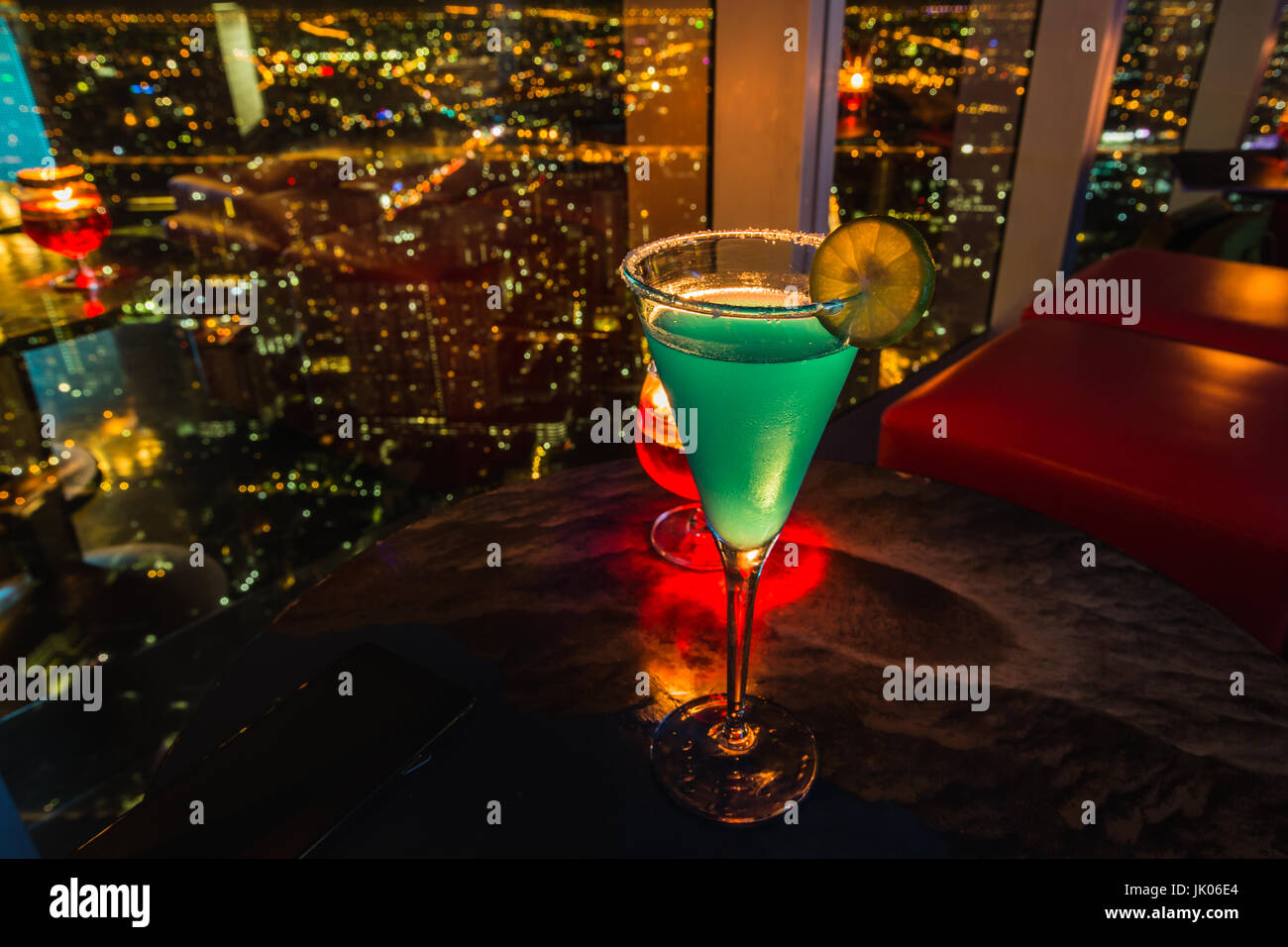 Illuminazione Lowkey e closeup messa a fuoco selettiva per cocktail e limone sulla parte superiore, un piccolo drink dopo cena con la sfocatura dello sfondo notturno della città sul grattacielo Foto Stock