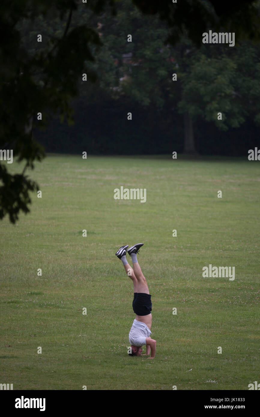Un capovolto l uomo rimane bilanciato sulla sua testa in un parco pubblico - uno in una sequenza di quattro - il 19 luglio 2017, in Ruskin Park, South London borough di Lambeth, Inghilterra. Foto Stock