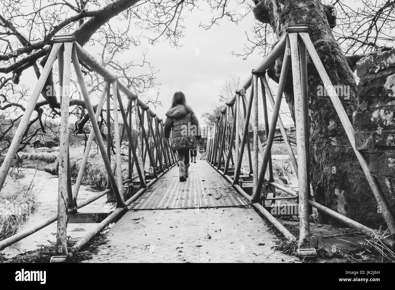 Un vecchio stile fotografia in bianco e nero di una giovane ragazza camminare attraverso un ponte metallico su una passeggiata in campagna Foto Stock