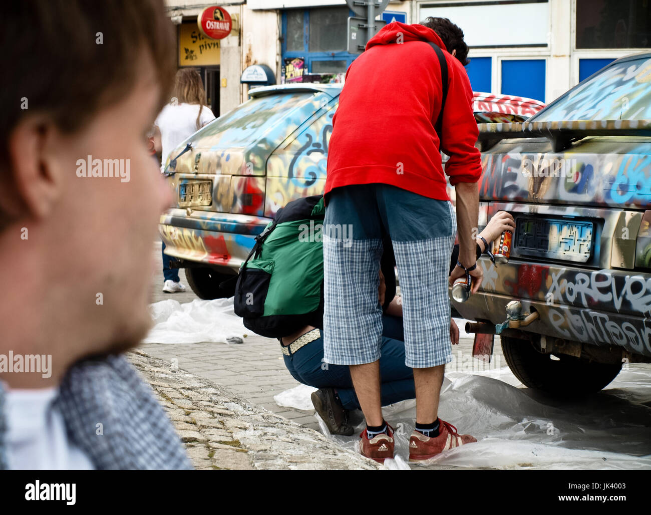 I giovani la spruzzatura su vecchie automobili parcheggiate in strada, graffiti in azione Foto Stock