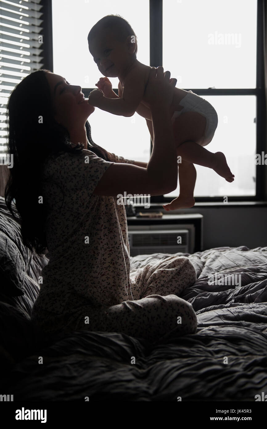 Madre caucasica seduta sul letto baby sollevamento figlio Foto Stock
