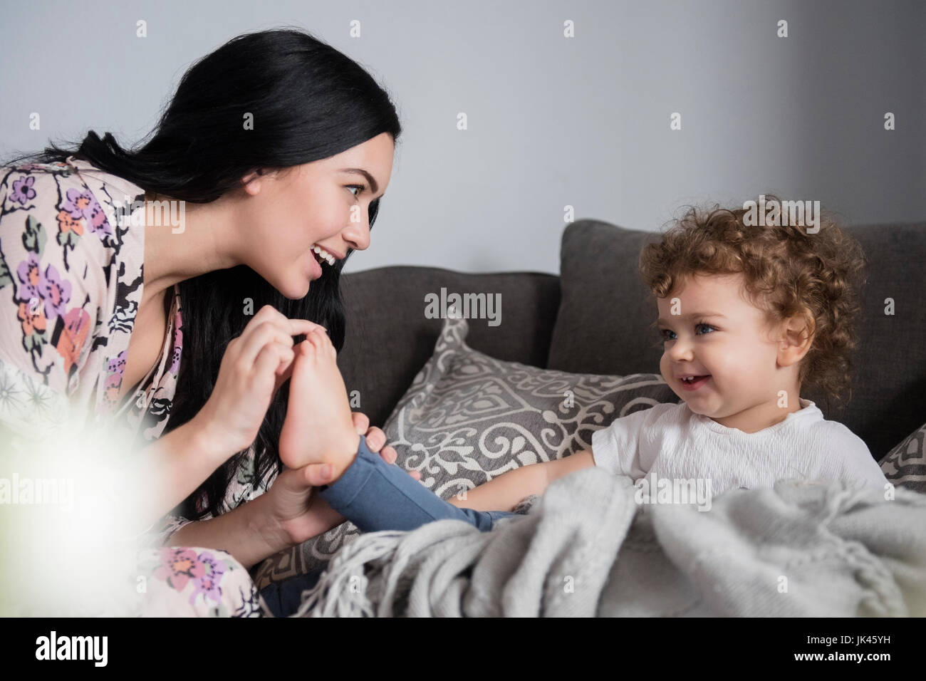 Madre caucasica seduti sul divano a giocare con le dita dei piedi del figlio Foto Stock