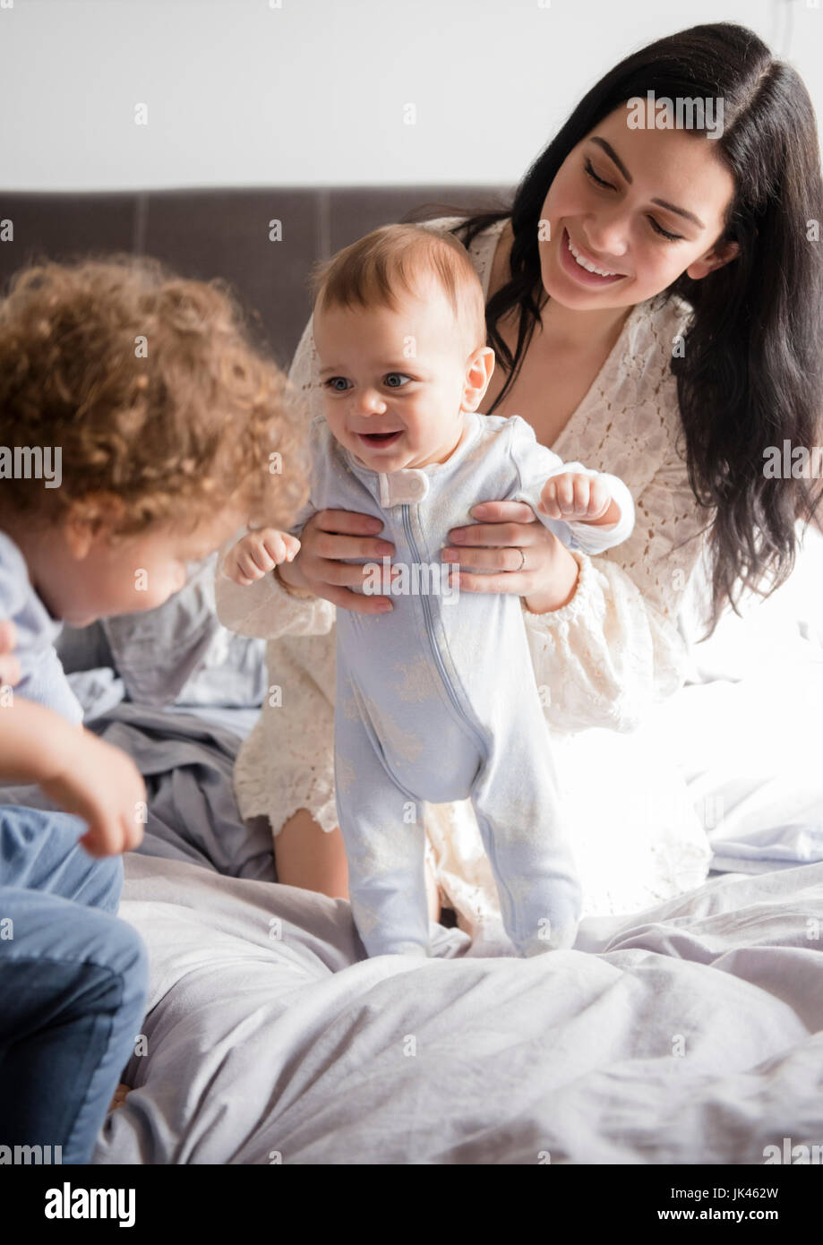 Madre caucasica inginocchiato sul letto a giocare con figli Foto Stock