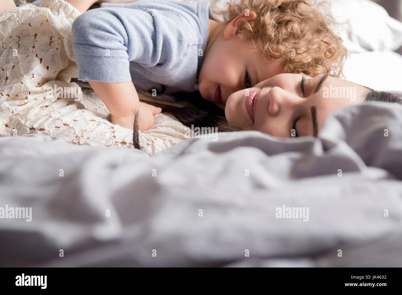 Madre caucasica la posa sul letto abbracciando il figlio Foto Stock