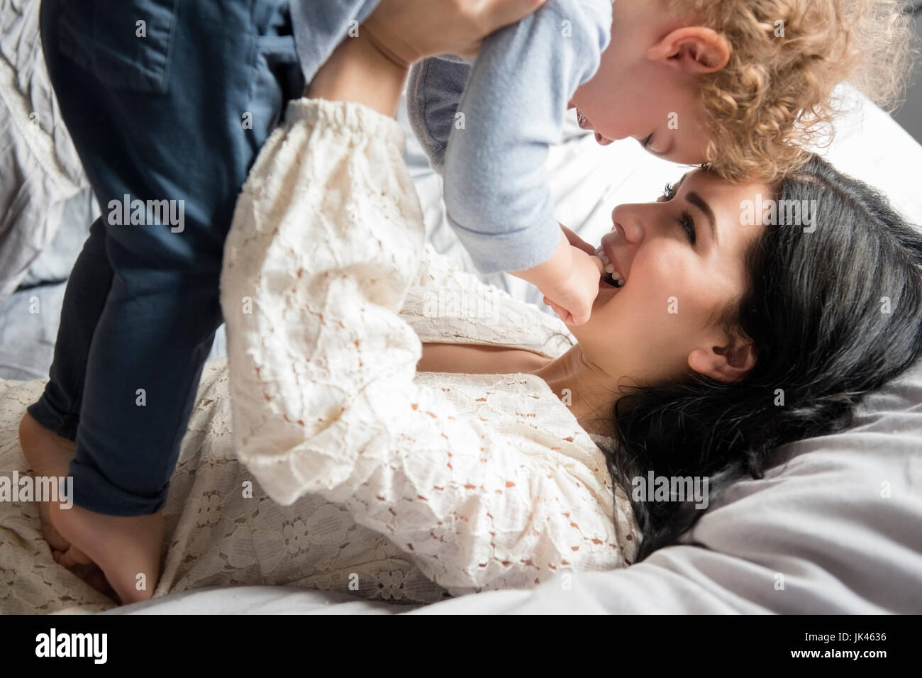 Madre caucasica la posa sul letto figlio di sollevamento Foto Stock