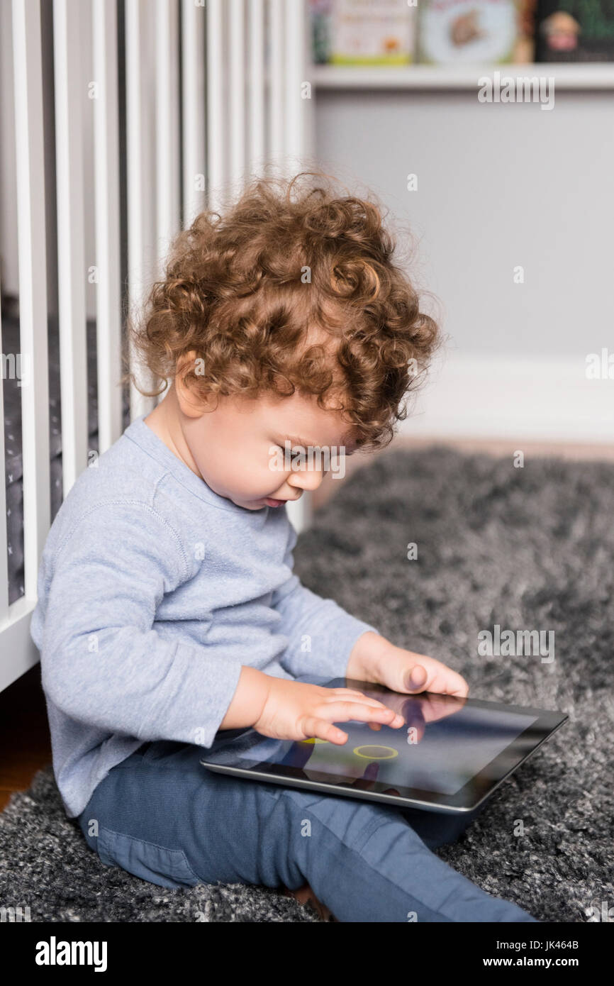 Caucasian ragazzo seduto sul pavimento a giocare con tavoletta digitale Foto Stock