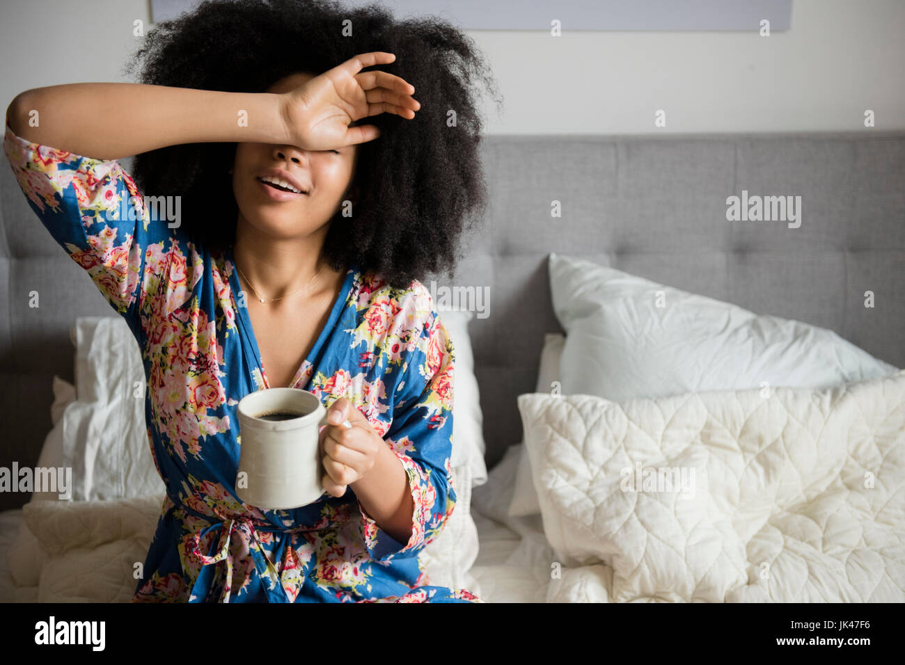 African American donna seduta nel letto di bere il caffè Foto Stock
