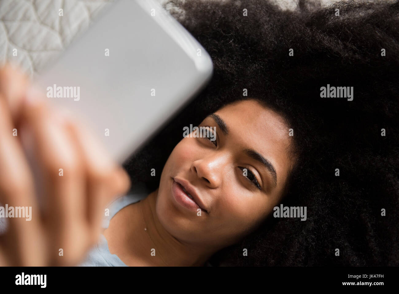 African American donna posa nel letto i messaggi di testo sul telefono cellulare Foto Stock
