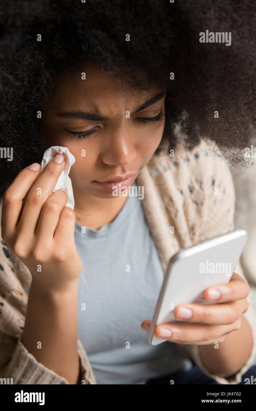 African American donna che piange e i messaggi di testo sul telefono cellulare Foto Stock